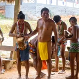 Grupo de hombres y niños indígenas tocando instrumentos tradicionales al aire libre y celebrando su herencia cultural.