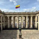 The Colombian flag waves above a historic courtyard in Bogotá, Colombia, under a clear sky.