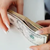 Hands carefully holding a stack of US dollar bills, representing finance and currency.