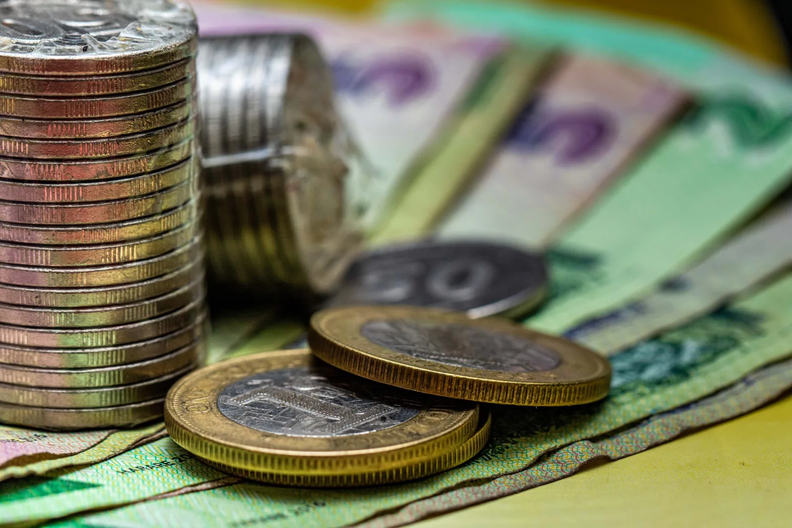 Imagen de primer plano de monedas apiladas y varias notas de moneda, representando conceptos financieros.