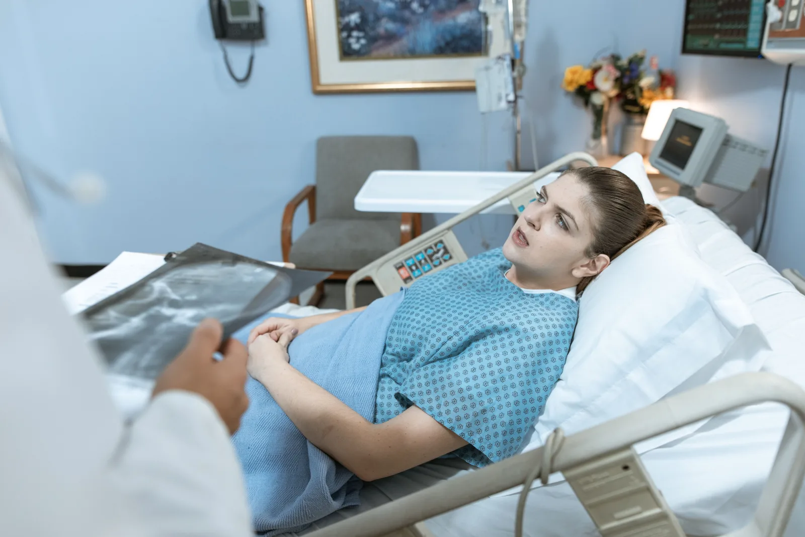 Mujer caucásica en una cama de hospital recibiendo atención de un profesional sanitario.