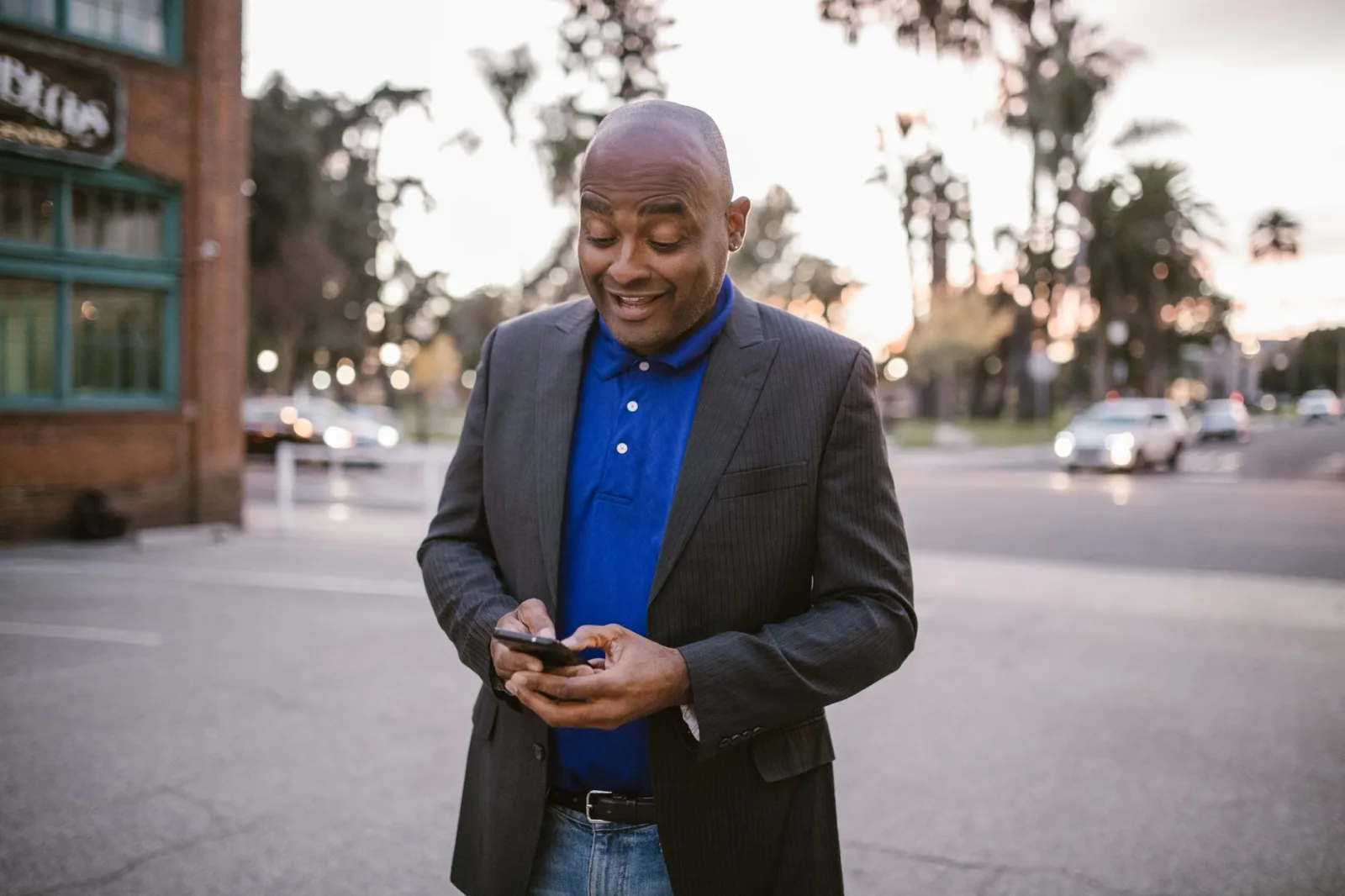 Un hombre adulto con traje usa felizmente su teléfono inteligente al aire libre al atardecer, mostrando la comunicación y un estilo de vida moderno.