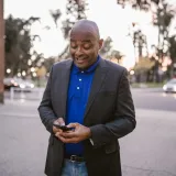 Un hombre adulto con traje usa felizmente su teléfono inteligente al aire libre al atardecer, mostrando la comunicación y un estilo de vida moderno.