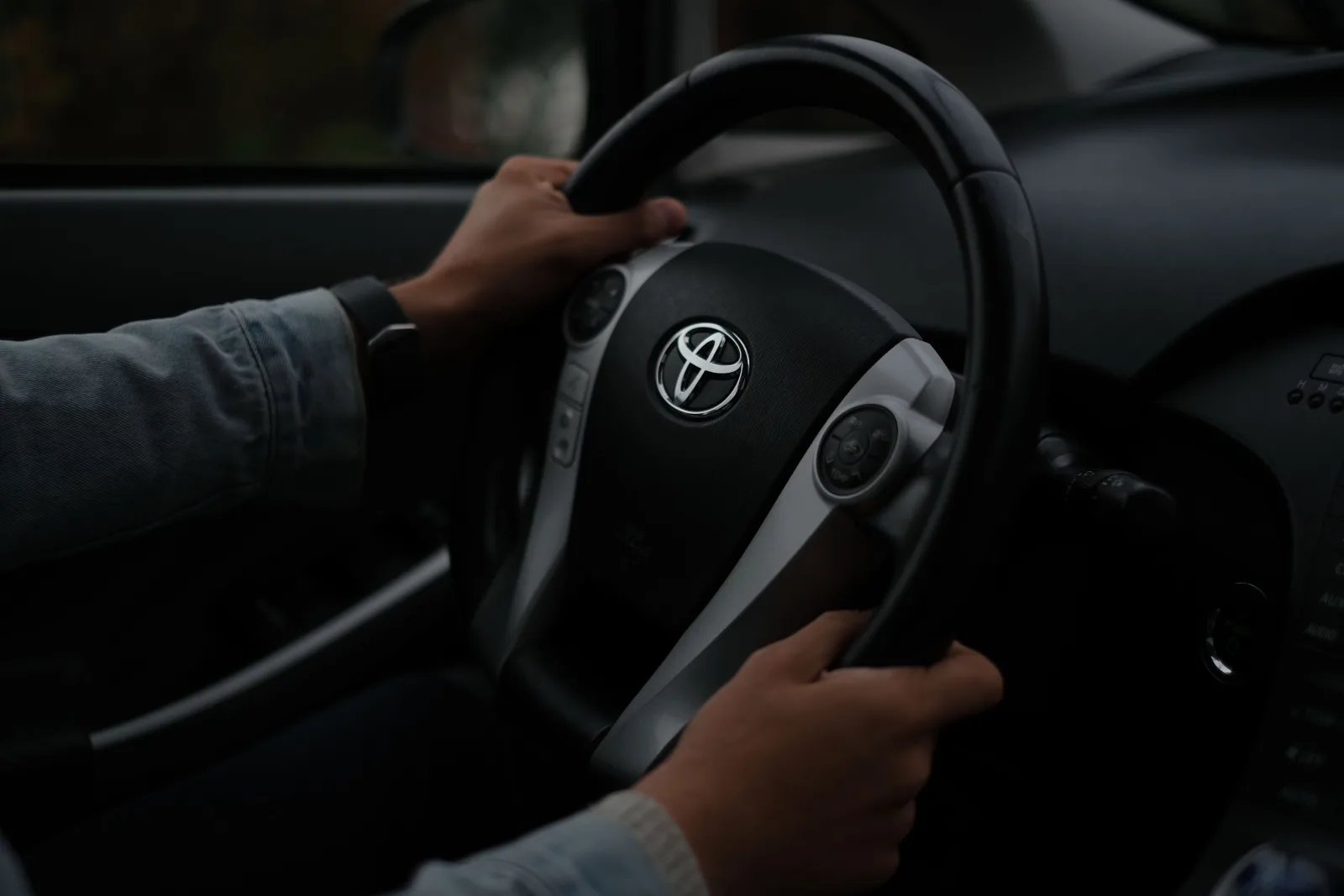 Manos sobre el volante de un Toyota, en primer plano dentro de un vehículo. Ambiente oscuro.