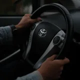Manos sobre el volante de un Toyota, en primer plano dentro de un vehículo. Ambiente oscuro.