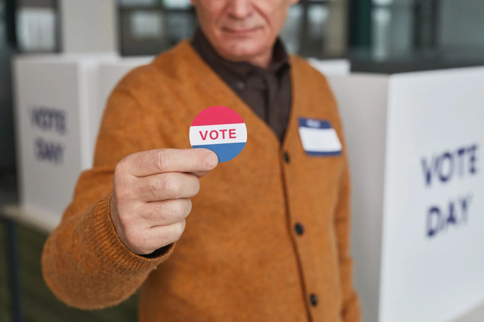 Una persona mayor sostiene una pegatina de votación dentro de una cabina electoral durante la jornada electoral.