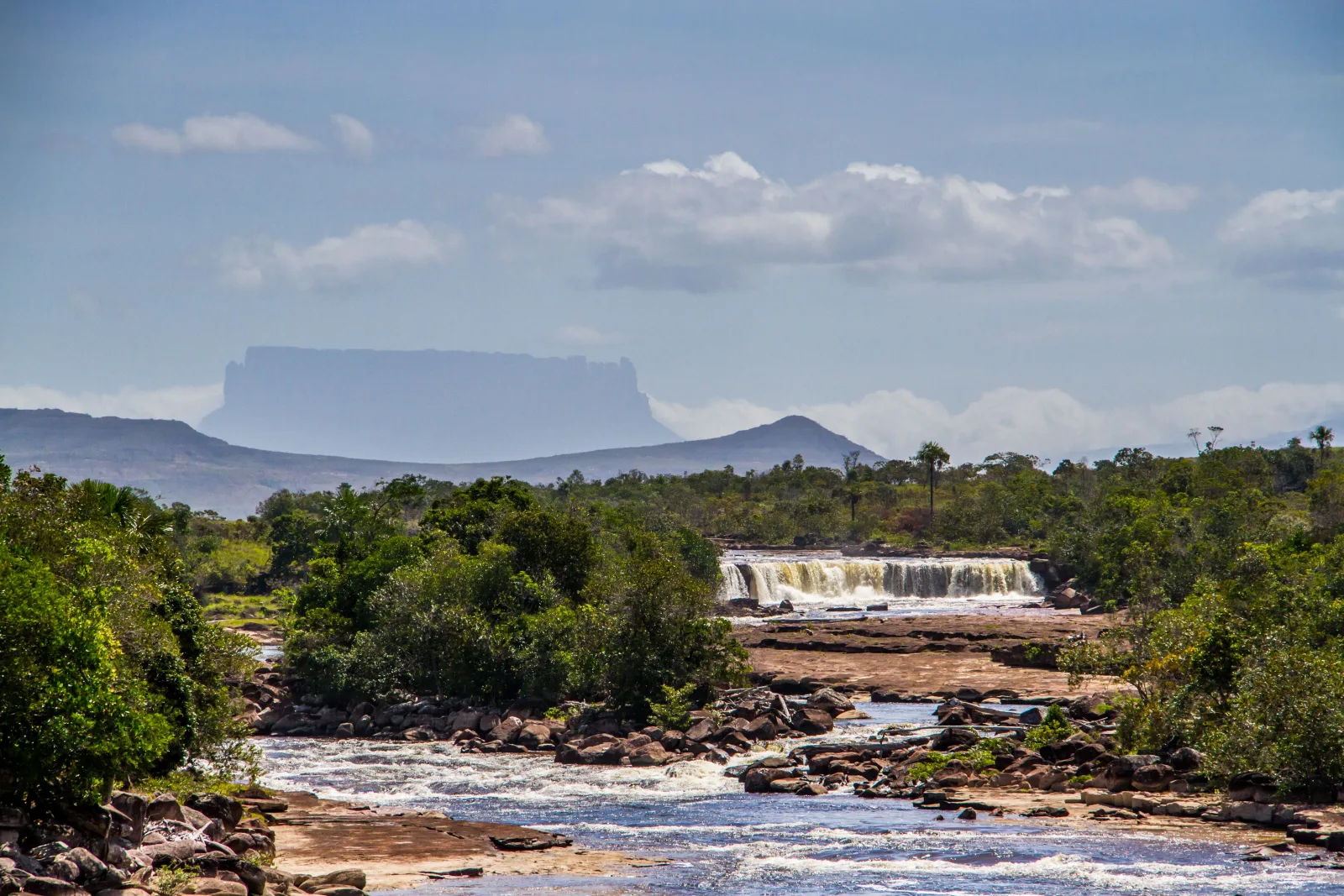 Impresionante vista de una cascada rodeada de exuberante vegetación y un tepuy al fondo, en el Parque Nacional Canaima, Venezuela.