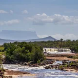 Impresionante vista de una cascada rodeada de exuberante vegetación y un tepuy al fondo, en el Parque Nacional Canaima, Venezuela.