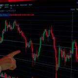 Mano señalando un gráfico del precio de Bitcoin en una pantalla, destacando las tendencias del mercado y el análisis de inversiones.