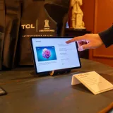 Una persona usando una tableta con pantalla táctil en una exposición tecnológica que muestra productos de TCL.