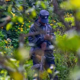 Un oficial de seguridad uniformado de pie en un entorno de vibrante y verde bosque, sosteniendo un arma.