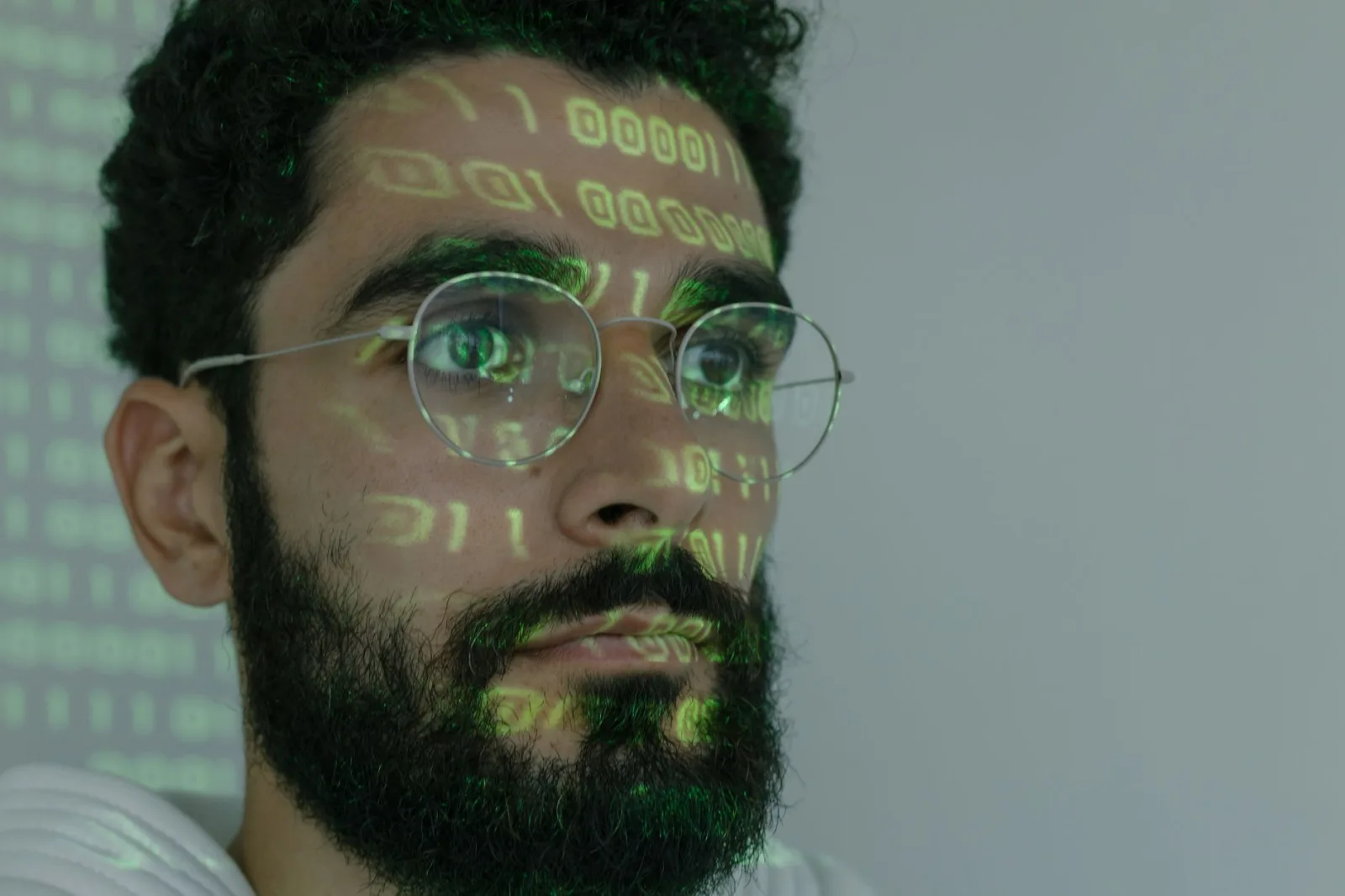 Un hombre barbudo con código binario digital proyectado en el rostro, que simboliza la ciberseguridad y la tecnología.