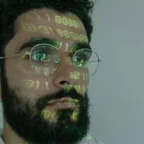 Un hombre barbudo con código binario digital proyectado en el rostro, que simboliza la ciberseguridad y la tecnología.