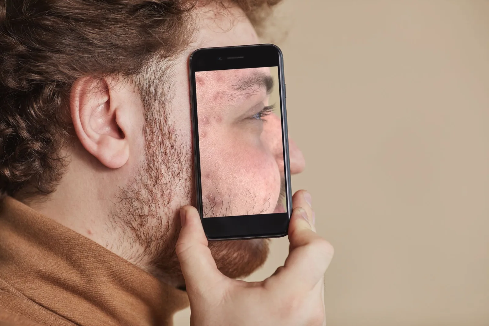 Un hombre adulto sostiene un teléfono inteligente que muestra el reflejo de su rostro, como ejemplo de fotografía creativa con el móvil.