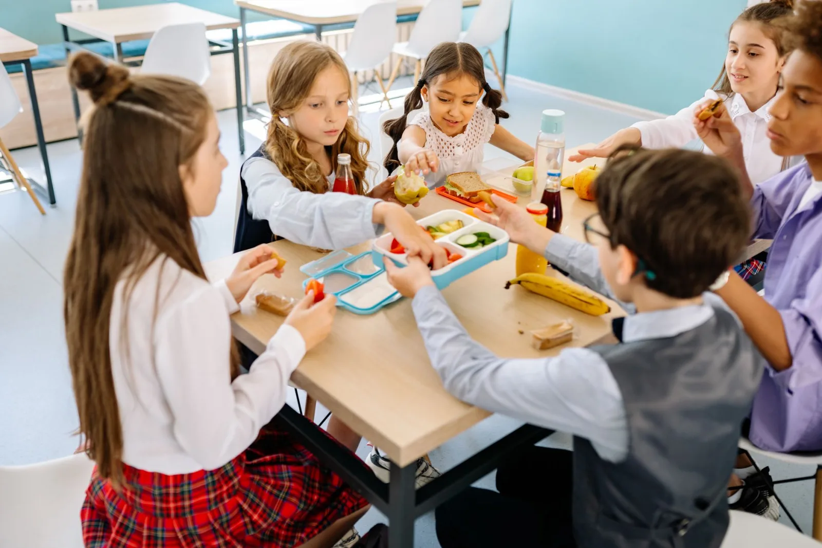 Grupo de niños diversos almorzando en el comedor escolar, compartiendo y disfrutando de refrigerios saludables.