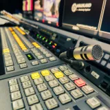 Vista detallada del panel de control de un estudio de transmisión con un micrófono y varias pantallas.
