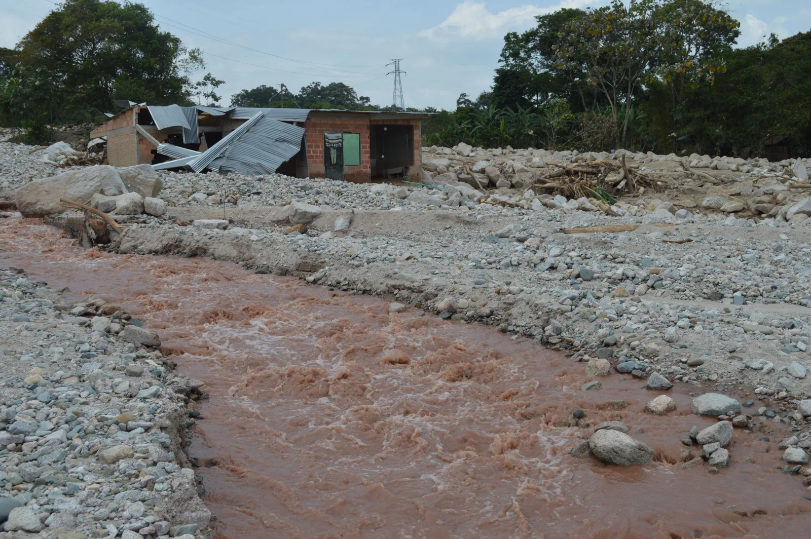 Una casa dañada se encuentra junto a un río lodoso después de una inundación, lo que ilustra el impacto de los desastres naturales.