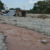 Una casa dañada se encuentra junto a un río lodoso después de una inundación, lo que ilustra el impacto de los desastres naturales.