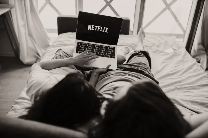 Una pareja relajándose juntos, viendo Netflix en una laptop en una habitación acogedora.