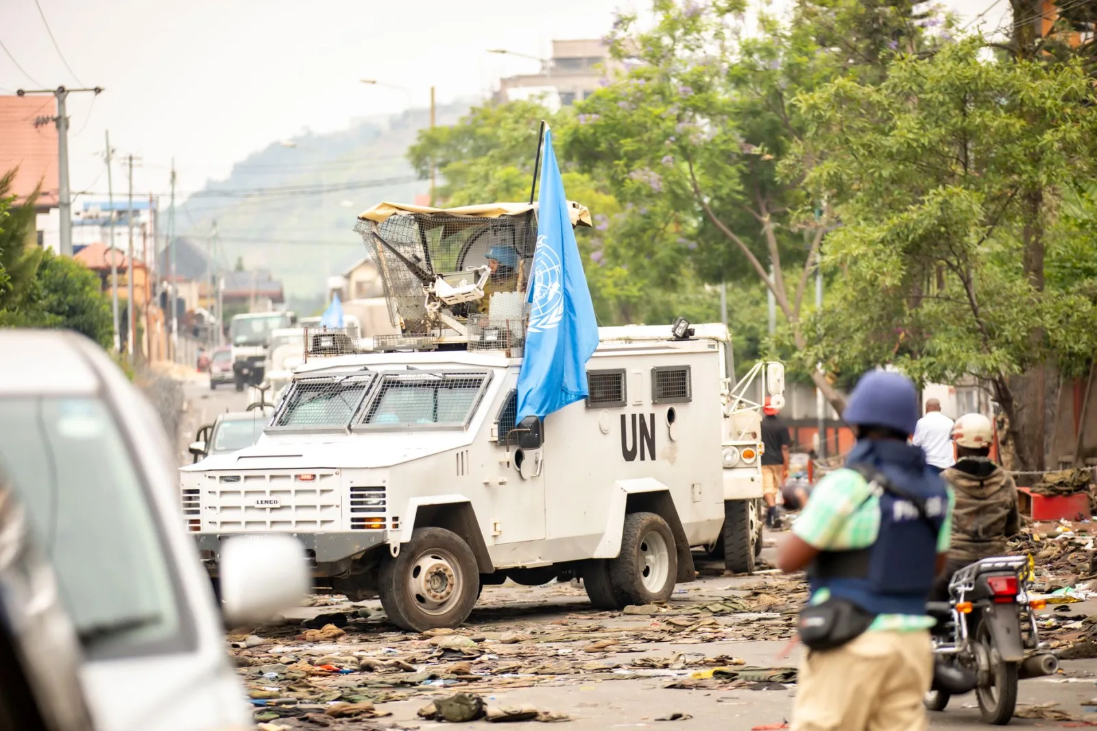 Vehículo blindado de las Naciones Unidas avanzando por una calle en medio del conflicto. Presencia de paz y seguridad.