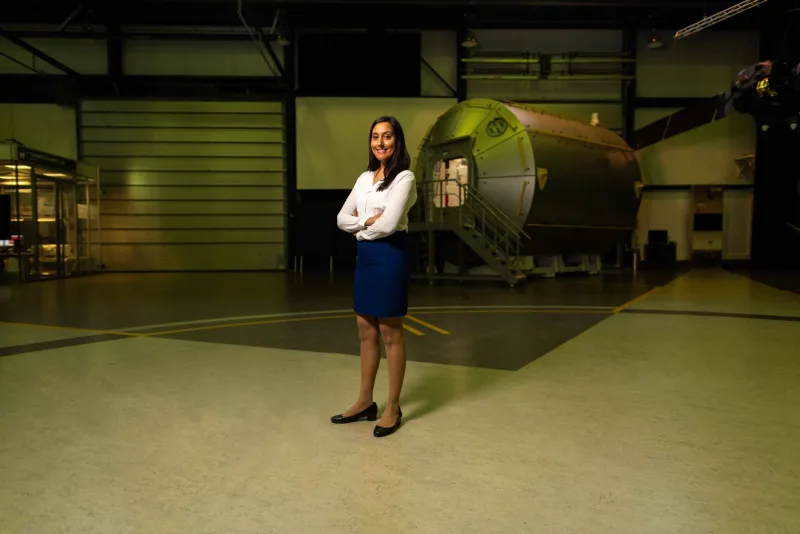 A professional female engineer stands confidently in a spacecraft hangar, showcasing intelligence and pride.