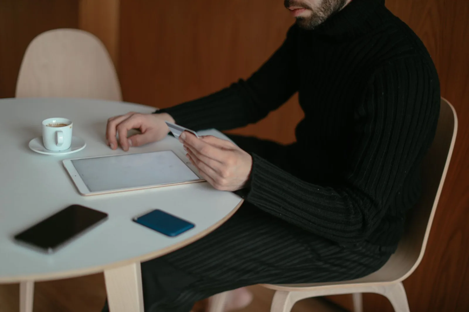 Hombre adulto usando tablet y tarjeta de crédito para comprar en línea en casa, sentado junto a la mesa con café.