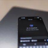 Primer plano de un smartphone con la interfaz de un asistente de inteligencia artificial en la pantalla, sobre un portátil.