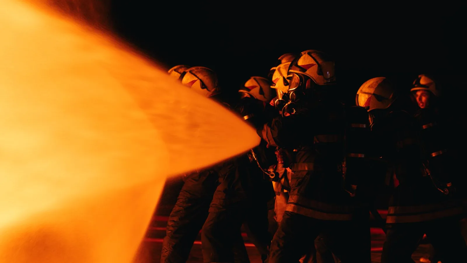 Un grupo de bomberos con equipo de protección combate las llamas durante una operación nocturna.