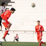 Jugadores de fútbol luchan por el balón en el aire durante un emocionante partido al aire libre.