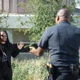 A police officer engages with a civilian raising hands outdoors, signifying communication or questioning.