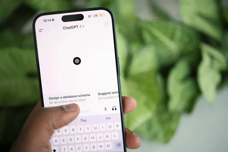 Mano sosteniendo un smartphone que muestra la interfaz de ChatGPT, rodeada de vegetación.