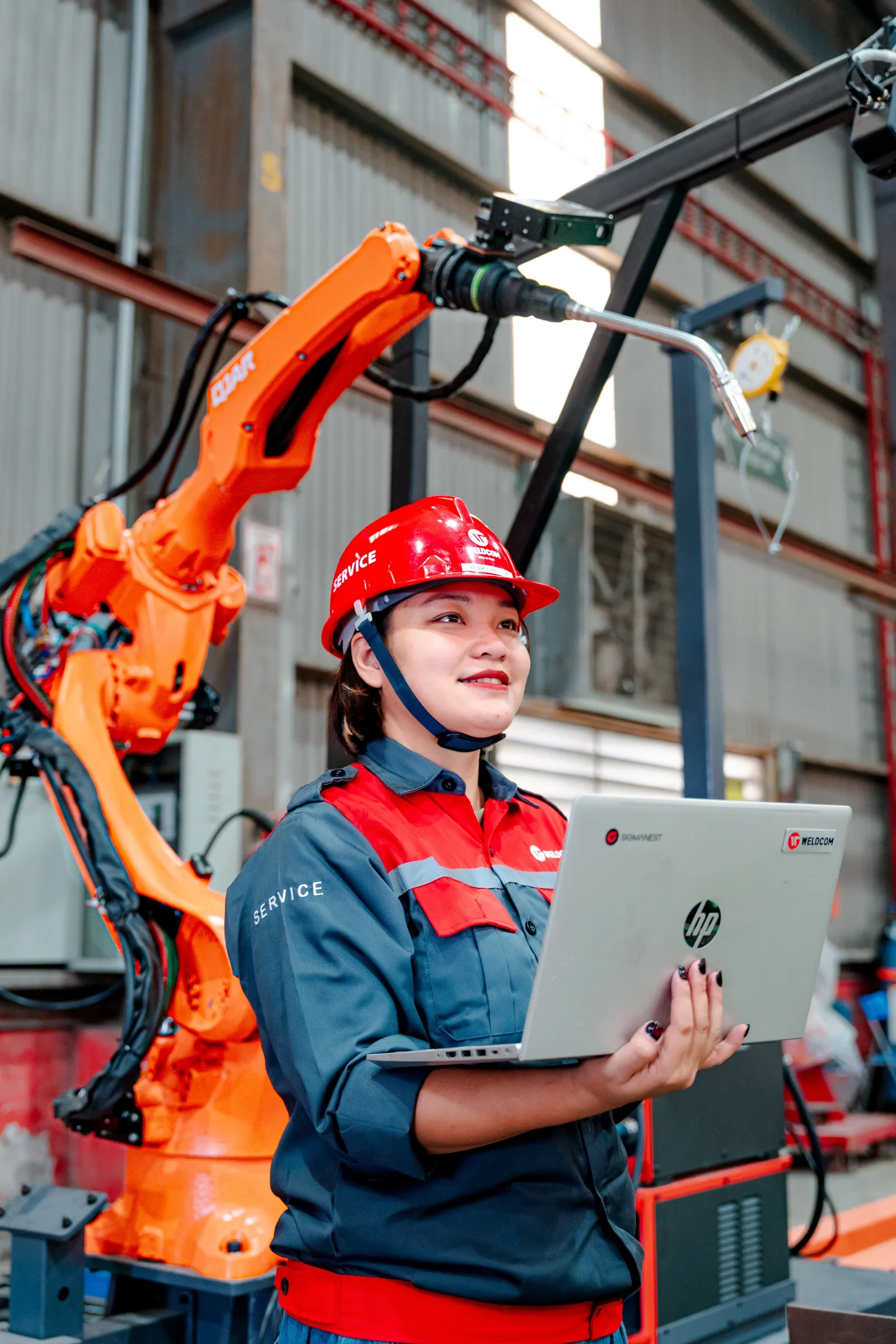 Ingeniera supervisando un brazo robótico con una computadora portátil en una planta de fabricación en Vietnam.