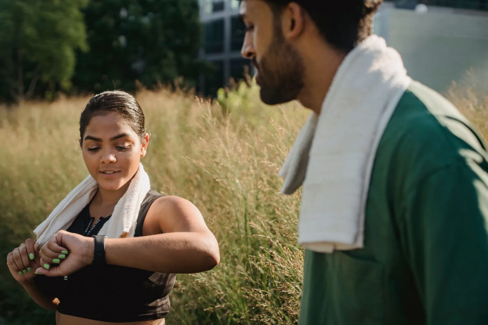 Una pareja al aire libre usa monitores de actividad física después de entrenar, con toallas puestas.