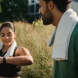 Una pareja al aire libre usa monitores de actividad física después de entrenar, con toallas puestas.