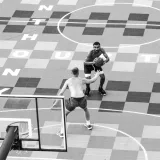 Vista desde un ángulo alto de hombres sin camisa jugando baloncesto en una cancha urbana única.