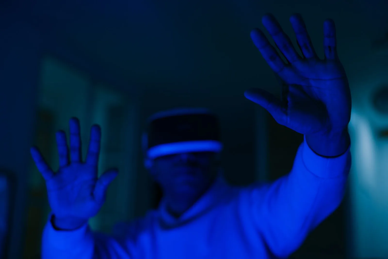 Hombre con casco de realidad virtual inmerso en realidad virtual con manos visibles en iluminación azul.