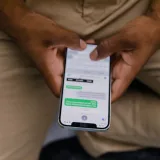 Primer plano de unas manos escribiendo mensajes en un teléfono inteligente, con el foco en la pantalla que muestra los mensajes.
