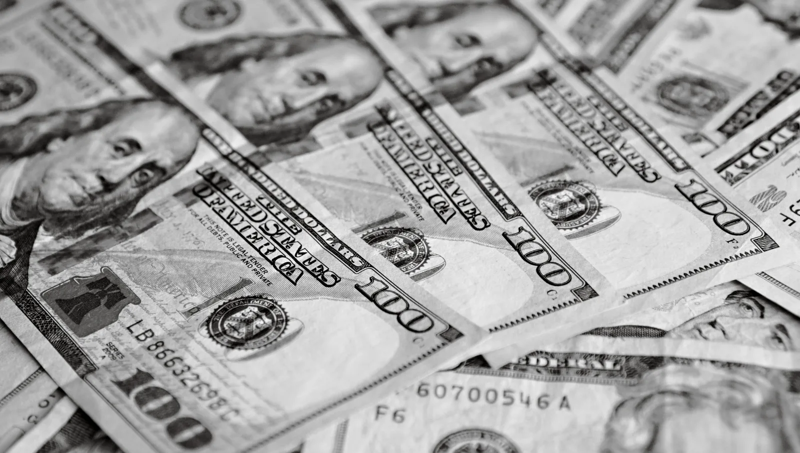 Un primer plano en blanco y negro de varios billetes de cien dólares estadounidenses esparcidos.