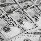 Un primer plano en blanco y negro de varios billetes de cien dólares estadounidenses esparcidos.