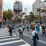 A large group of people in a city protest, wearing masks and carrying banners.