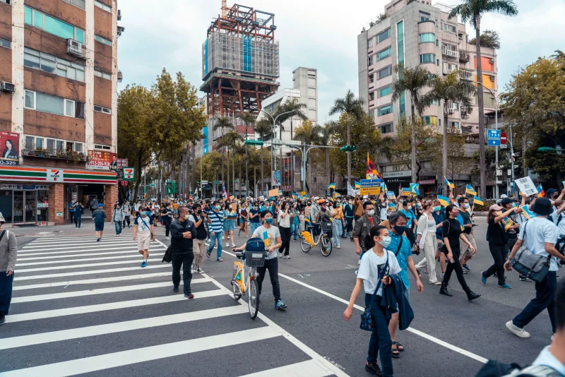 A large group of people in a city protest, wearing masks and carrying banners.