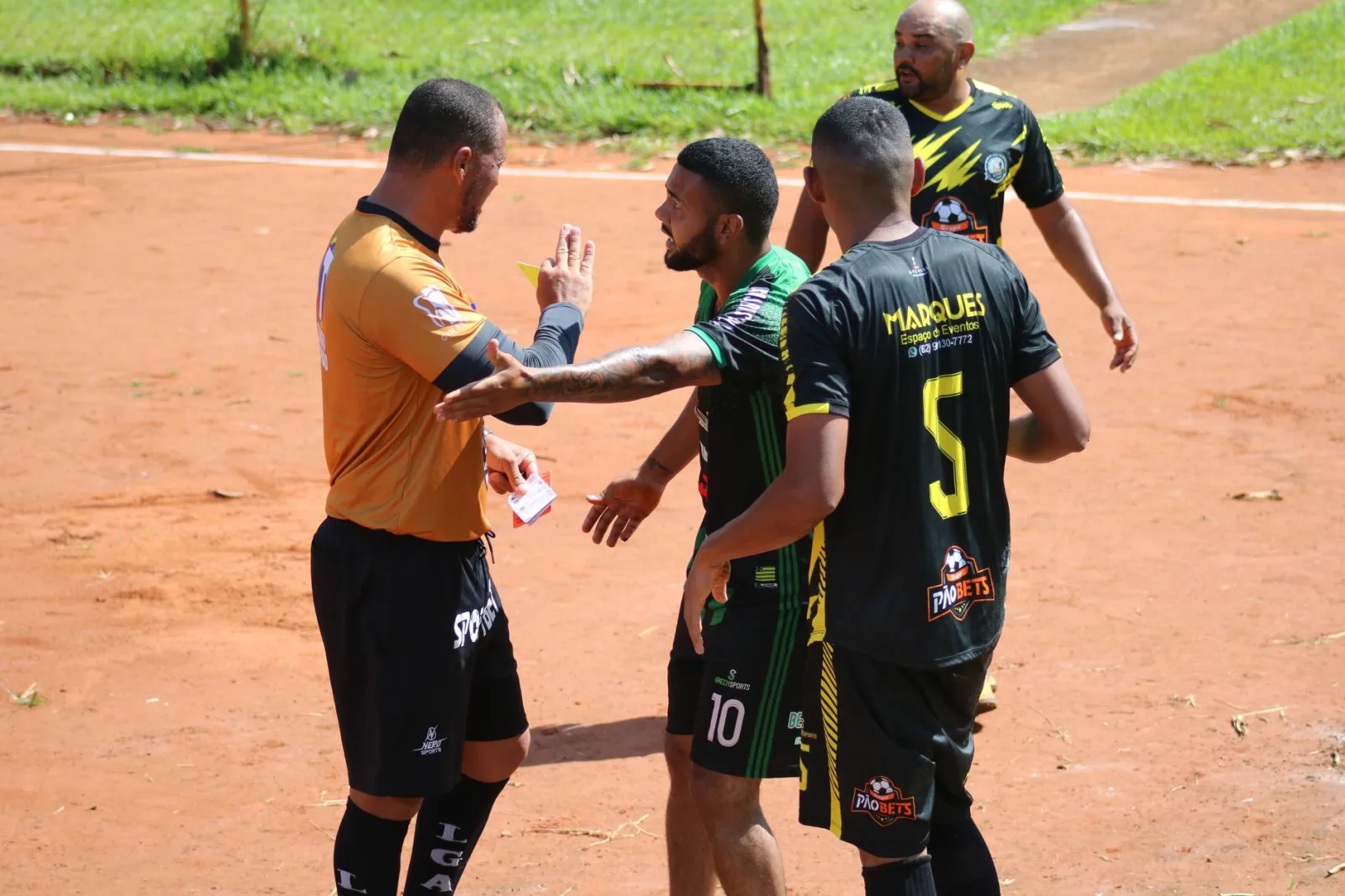 Un momento tenso en el campo mientras un árbitro le muestra una tarjeta a un jugador durante un partido de fútbol bajo el sol.