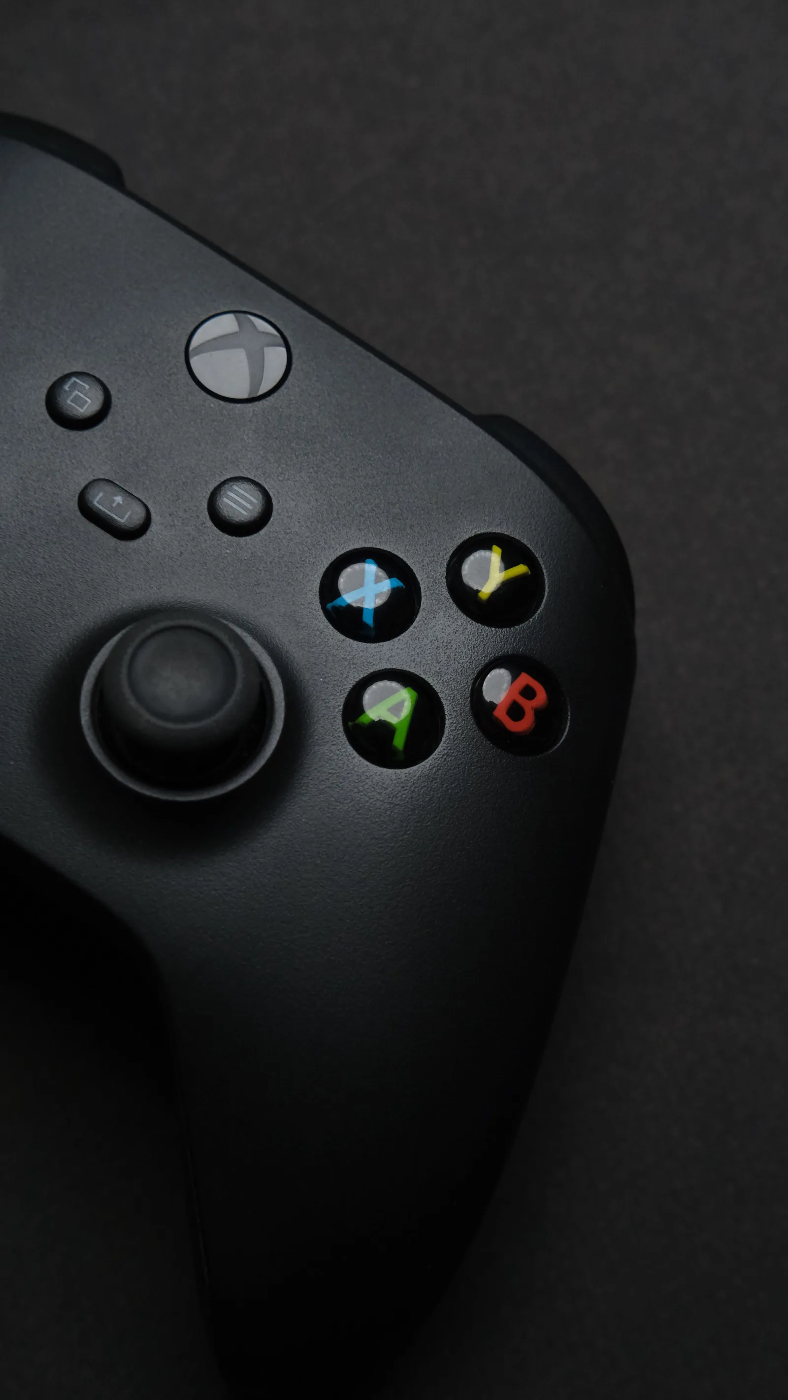 Primer plano de un control de videojuegos Xbox negro sobre un fondo oscuro, con los botones destacados.