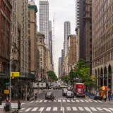 A busy street view of Midtown Manhattan with historic and modern buildings, pedestrians, and traffic.