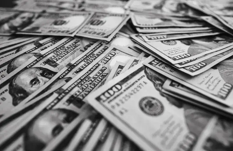 Monochrome image of scattered US hundred dollar bills representing wealth and prosperity.