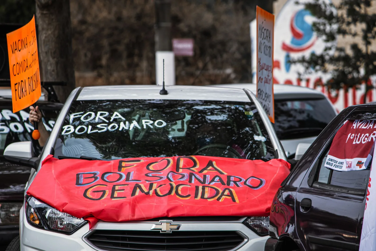 Autos mostrando carteles anti-Bolsonaro durante una protesta callejera, resaltando el activismo político.