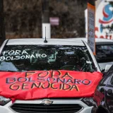 Autos mostrando carteles anti-Bolsonaro durante una protesta callejera, resaltando el activismo político.