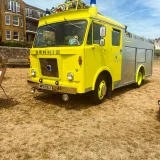 Un camión de bomberos Dennis vintage de color amarillo exhibido en un día soleado al aire libre, mostrando un diseño clásico.