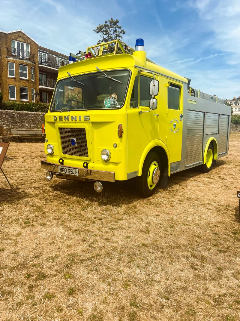 Un camión de bomberos Dennis vintage de color amarillo exhibido en un día soleado al aire libre, mostrando un diseño clásico.