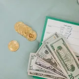 Primer plano de dólares estadounidenses y monedas de Bitcoin sobre un planificador de presupuesto semanal, que simbolizan las finanzas modernas.